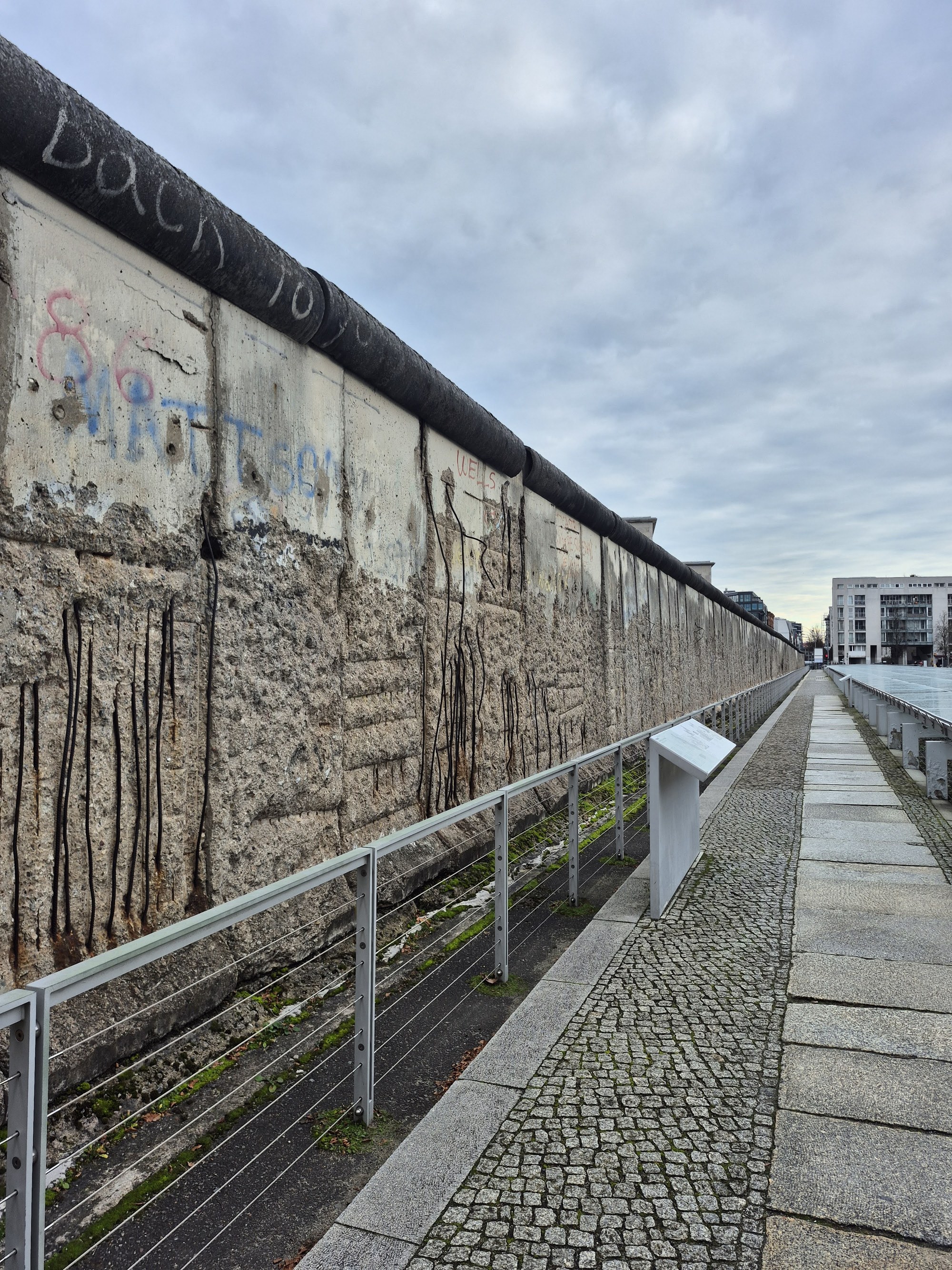 A surviving stretch of the Berlin Wall along Niederkirchnerstraße at the Topography of Terror, weathered concrete behind a low fence with the outdoor exhibition panels beside it