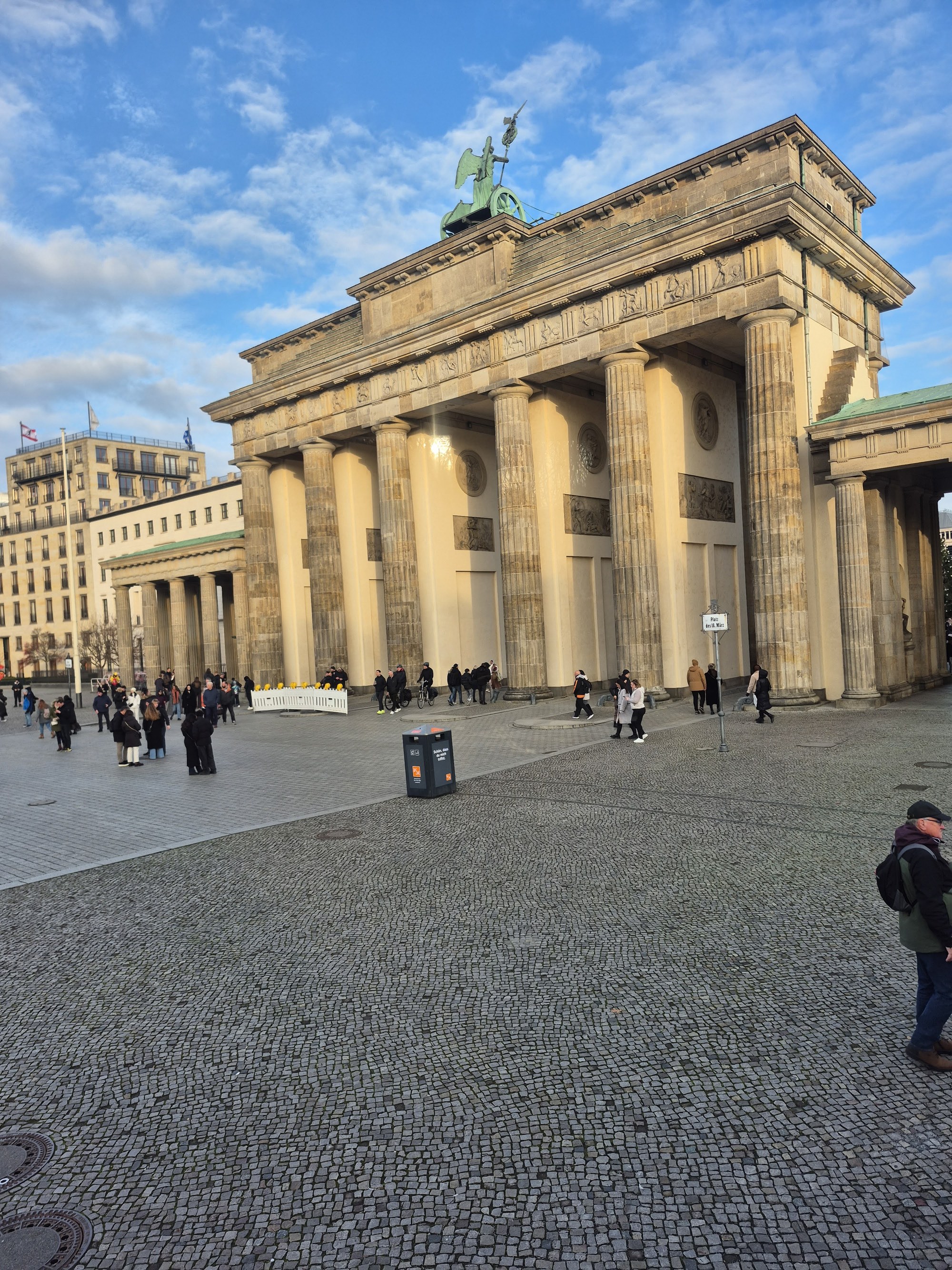 The Brandenburg Gate on a clear December afternoon, its six Doric columns and the Quadriga against a blue sky, a few people crossing the cobbled Pariser Platz