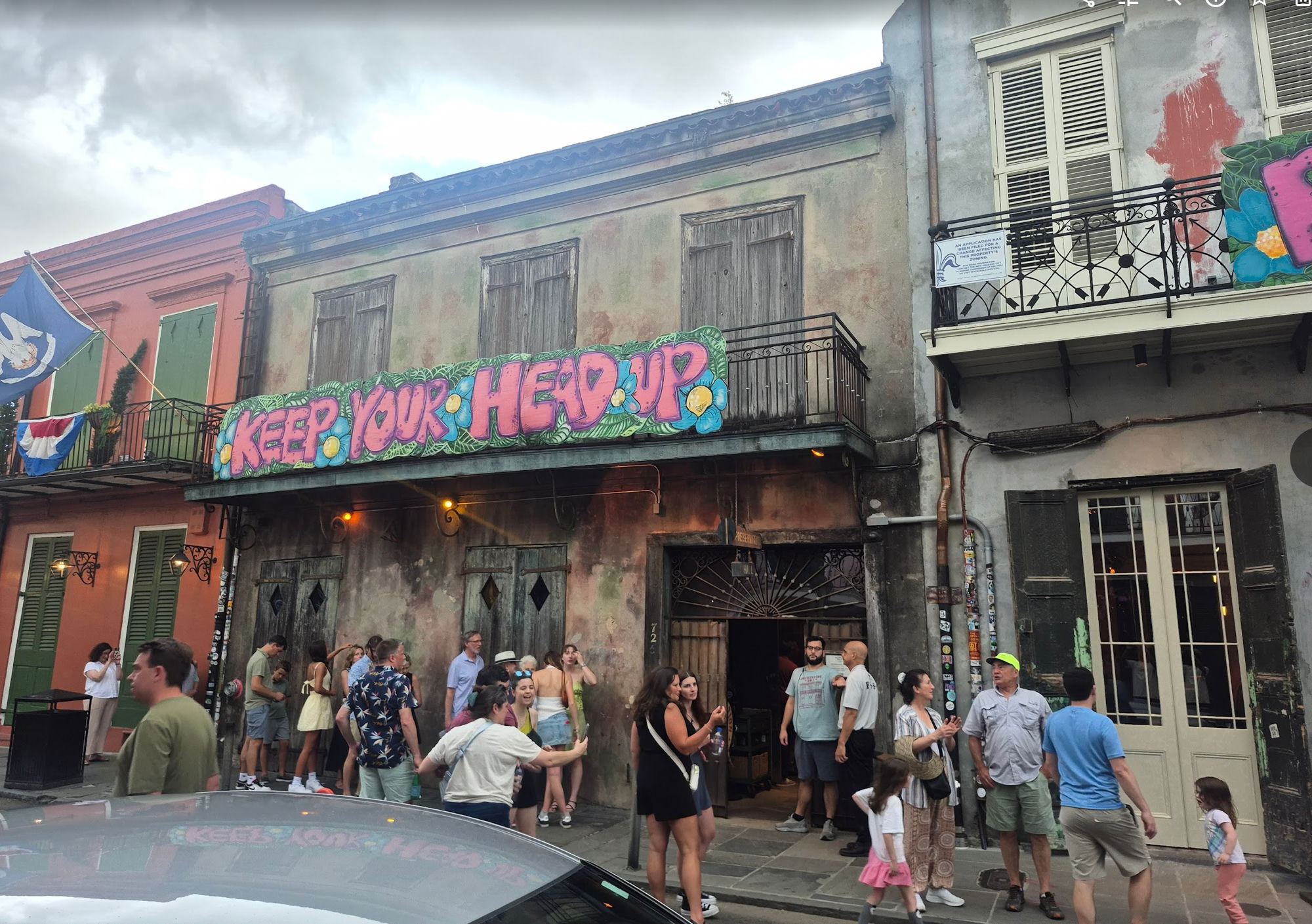 The weathered exterior of Preservation Hall in the French Quarter, a crowd gathered outside under a mural reading 'KEEP YOUR HEAD UP'