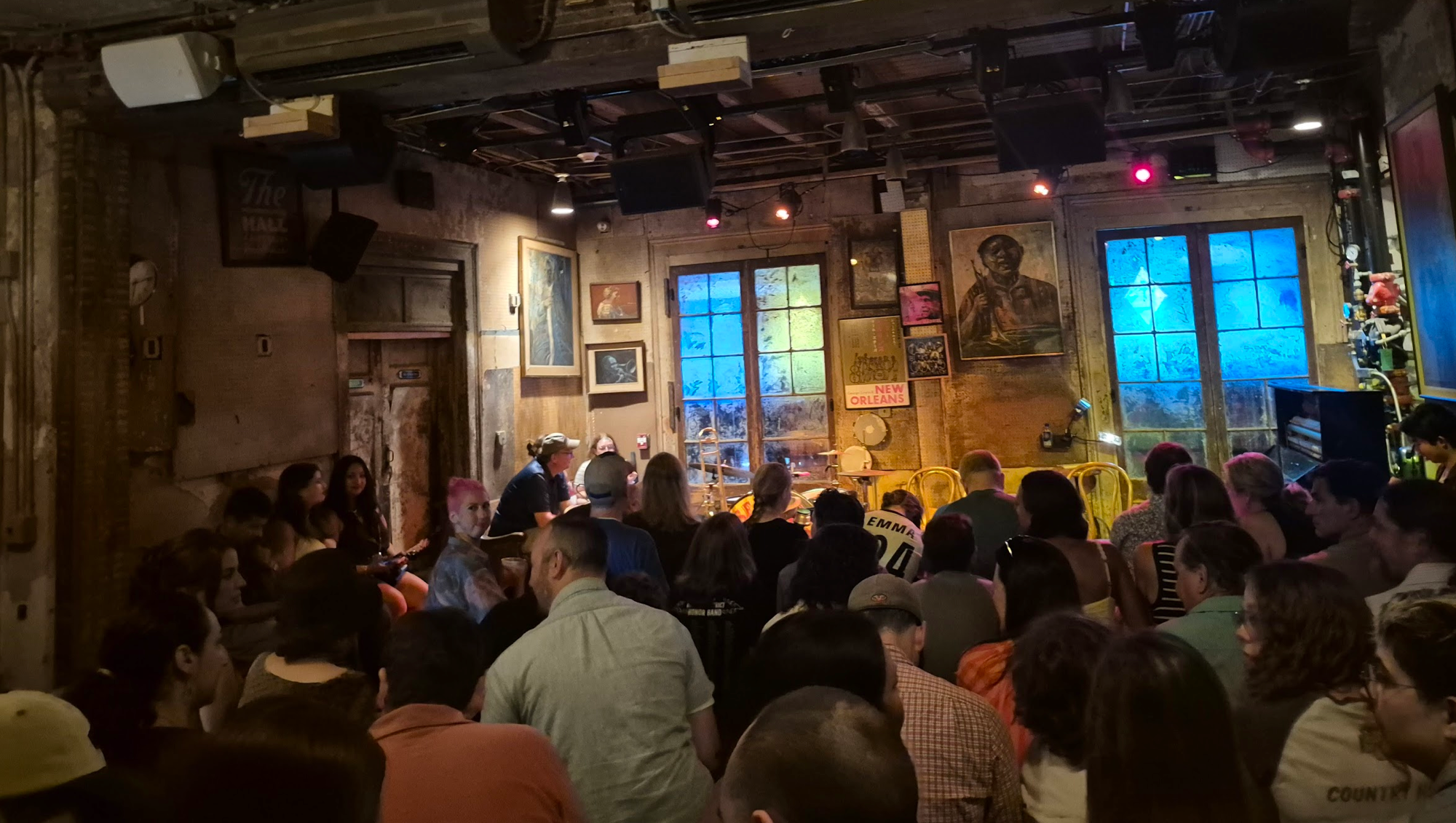 A packed crowd inside the dim, weathered room at Preservation Hall, New Orleans, facing the band area with paintings on the worn walls